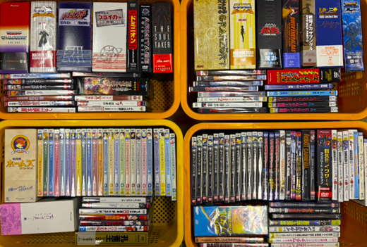 アニメや特撮関連のDVDボックスや単品ソフトが複数詰められた黄色いカゴ。90年代〜2000年代作品を中心とした大量買取品。
