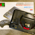セガの16ビットゲーム機「メガドライブ」本体と外箱。クラシックな黒い筐体が特徴の初代モデル。