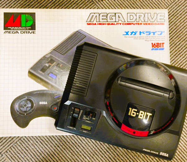 セガの16ビットゲーム機「メガドライブ」本体と外箱。クラシックな黒い筐体が特徴の初代モデル。